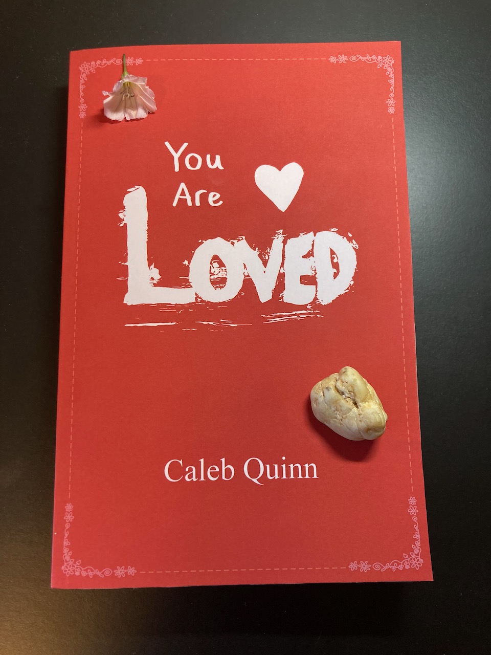The book "You Are Loved" with a rock and a flower